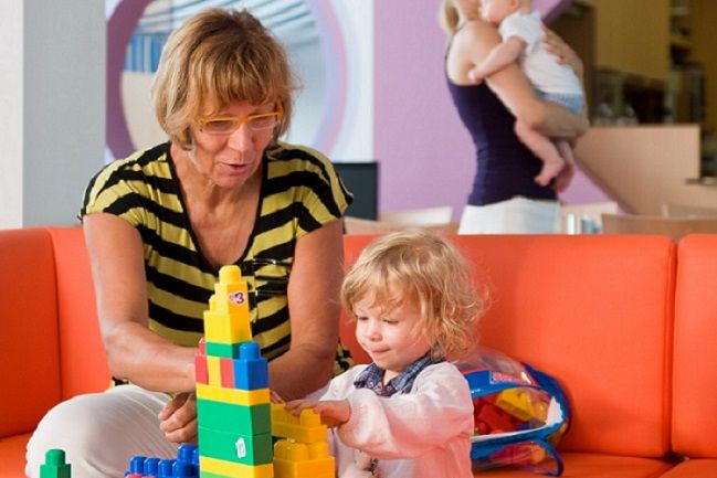 Eine Familienpatin kümmert sich liebevoll um ein Kleinkind, während die Mutter sich dem Säugling widmet – praktische Alltagshilfe und Entlastung für junge Familien.