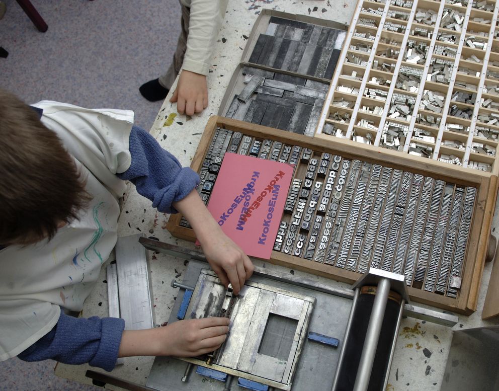 Ein Junge ordnet sorgfältig bewegliche Lettern, um einen Text für den Druck mit der Druckerpresse vorzubereiten