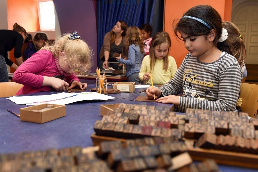 Children in a printing workshop composing their own stories using movable wooden letters – creative writing and printing at the after-school care center
