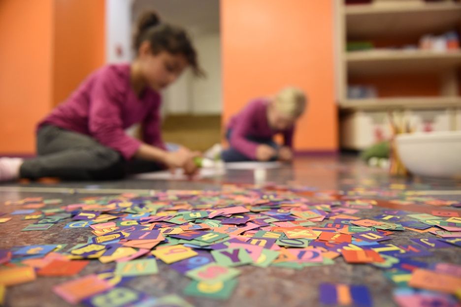 Zwei Kinder sitzen auf dem Fußboden und lösen gemeinsam ein buntes Sprachpuzzle zum Deutschlernen