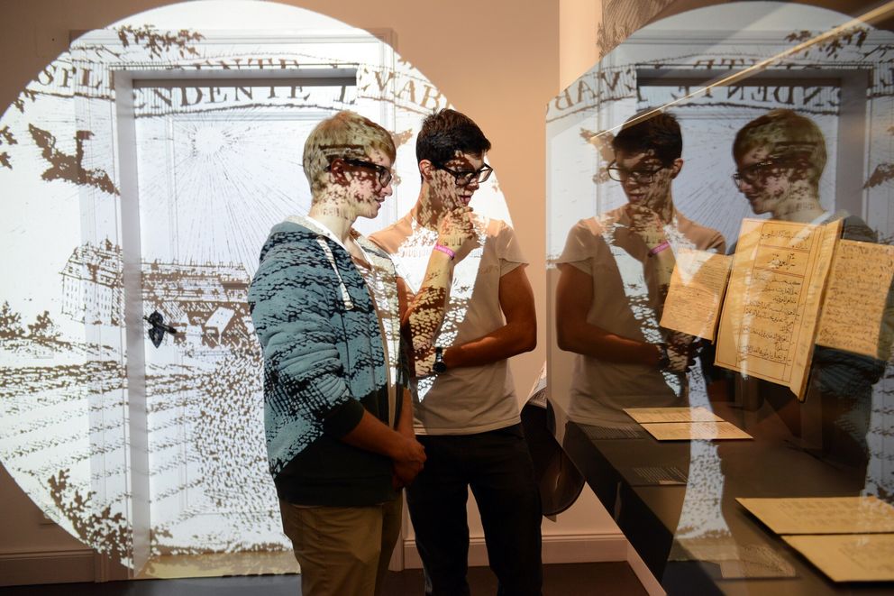 Zwei Besucher betrachten eine Vitrine mit fremdsprachigen Drucken aus dem 18. Jahrhundert, die die weltweite Verbreitung des Halleschen Pietismus dokumentieren, in den Franckeschen Stiftungen in Halle (Saale).